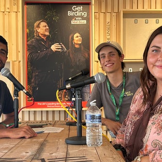 Three speakers seated around microphones during a live recording of the Wild Tales podcast at the Global Bird Fair.